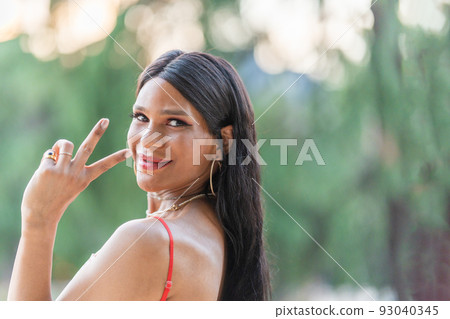 Trans woman gesturing victory with the fingers outdoors 93040345