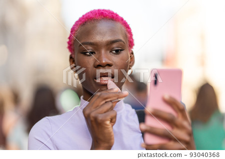 Afro woman applying cream to her lips using a mobile 93040368