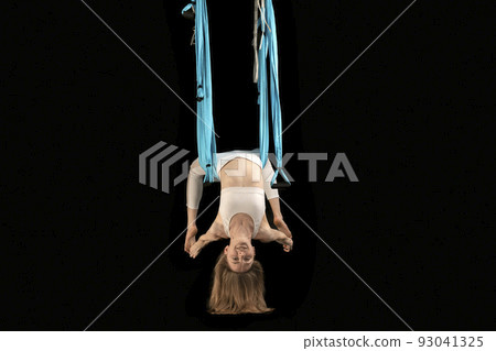 Yoga teacher performing antigravity yoga exercise. Young woman in white clothes does gymnastic tricks on blue canvas. 93041325