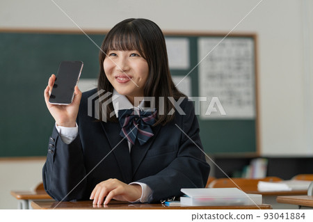 一個高中女生,在學校教室的休息時間里和朋友拿著智能手機聊天 一個高中女生,在學校教室的休息時間里和朋友拿著智能手機聊天 93041884