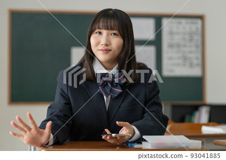 一個高中女生,在學校教室的休息時間里和朋友拿著智能手機聊天 一個高中女生,在學校教室的休息時間里和朋友拿著智能手機聊天 93041885