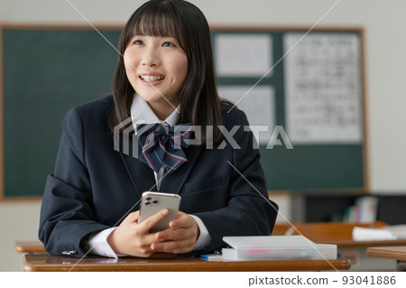 一個高中女生,在學校教室的休息時間里和朋友拿著智能手機聊天 一個高中女生,在學校教室的休息時間里和朋友拿著智能手機聊天 93041886