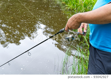 fisherman hand with spinning and reel on the summer lake, close-up. 93042927