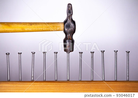 A few nails driven into the board and a small hammer on a light background A few nails driven into the board and a small hammer on a light background 93046017