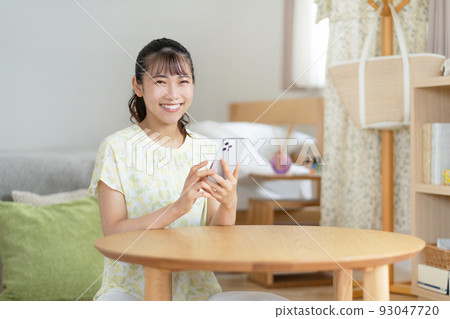 A young woman operating a smartphone in the living room A young woman operating a smartphone in the living room 93047720