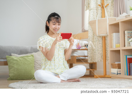 A young woman operating a smartphone in the living room A young woman operating a smartphone in the living room 93047721