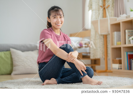 年輕女子坐在客廳的地板上微笑 93047836