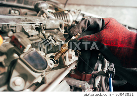 A auto mechanic is installing automobile iridium spark plugs into the ignition socket A auto mechanic is installing automobile iridium spark plugs into the ignition socket 93048031