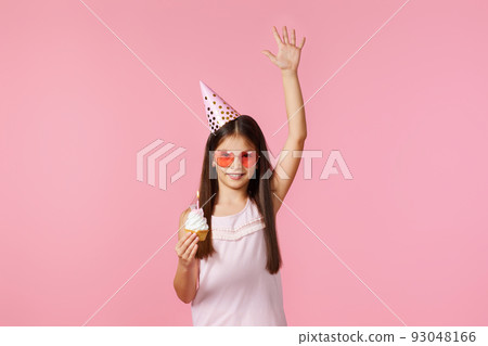 happy little birthday girl with party cone holding cupcake 93048166