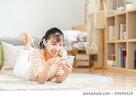 A young woman operating a smartphone in her room. A young woman operating a smartphone in her room. 93048429