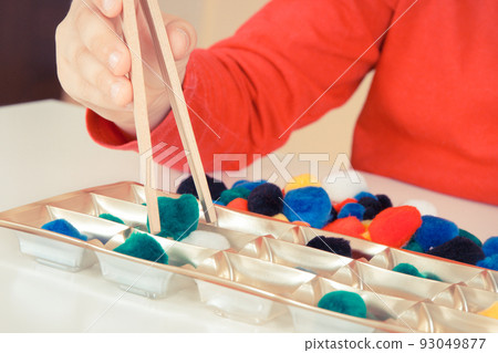 Preschooler playing with pompoms and wooden tongs. Development of kids motor skills 93049877