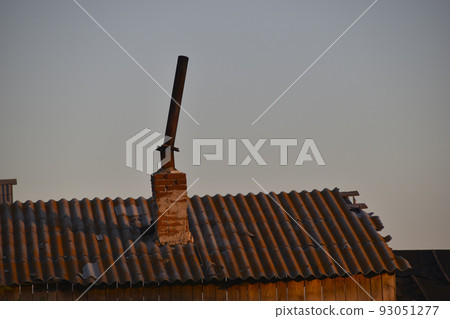 A crooked iron chimney in an old barn in the evening in the rays of the sun. A crooked iron chimney in an old barn in the evening in the rays of the sun. 93051277