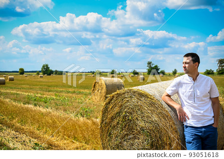 Happy farmer is standing beside bales of hay. He is examining st Happy farmer is standing beside bales of hay. He is examining st 93051618