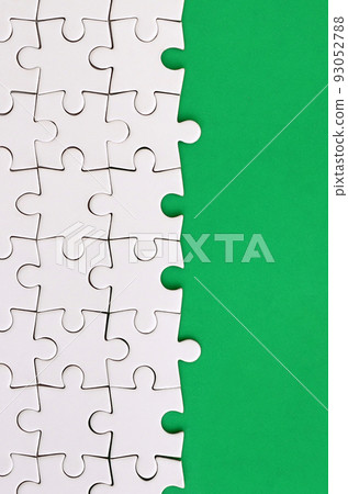 Fragment of a folded white jigsaw puzzle on the background of a green plastic surface. Texture photo with copy space for text Fragment of a folded white jigsaw puzzle on the background of a green plastic surface. Texture photo with copy space for text 93052788