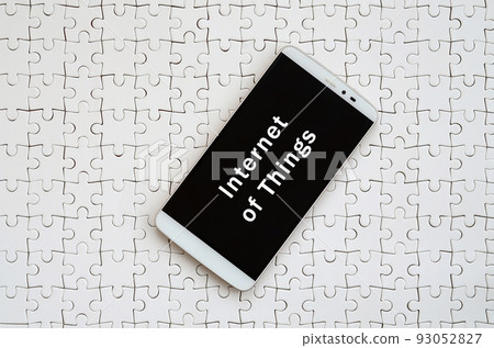 A modern big smartphone with a touch screen lies on a white jigsaw puzzle in an assembled state with inscription. Internet of things A modern big smartphone with a touch screen lies on a white jigsaw puzzle in an assembled state with inscription. Internet of things 93052827
