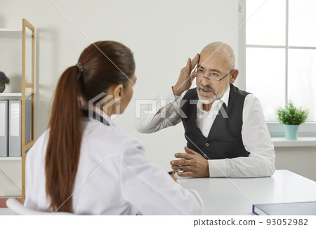 Older man during visit or consultation at clinic tells doctor about his severe headaches. 93052982
