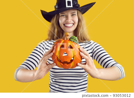 Small decorative pumpkin with funny face carved in Halloween style in hands of cheerful woman. Small decorative pumpkin with funny face carved in Halloween style in hands of cheerful woman. 93053012