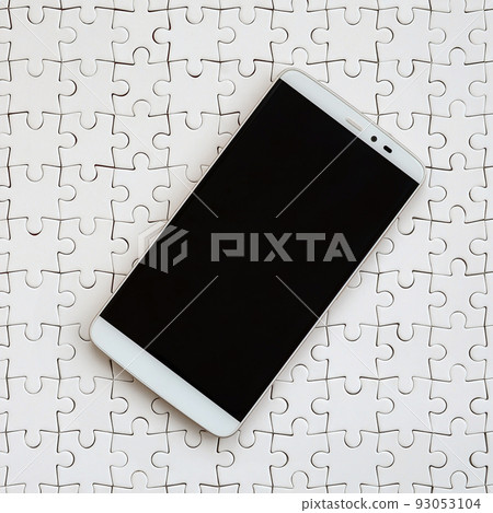 A modern big smartphone with a touch screen lies on a white jigsaw puzzle in an assembled state A modern big smartphone with a touch screen lies on a white jigsaw puzzle in an assembled state 93053104