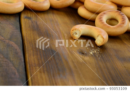 A lot of fresh yellow bagels lie on the surface of the old dark wood. A popular kind of flour products. One of the traditional Russian treats for tea A lot of fresh yellow bagels lie on the surface of the old dark wood. A popular kind of flour products. One of the traditional Russian treats for tea 93053109