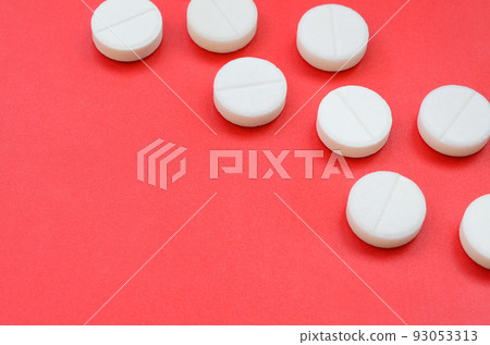 A few white tablets lie on a bright red background surface. Background image on medical and pharmaceutical topics 93053313