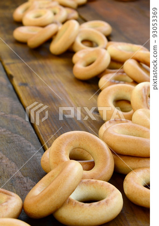 A lot of fresh yellow bagels lie on the surface of the old dark wood. A popular kind of flour products. One of the traditional Russian treats for tea A lot of fresh yellow bagels lie on the surface of the old dark wood. A popular kind of flour products. One of the traditional Russian treats for tea 93053369