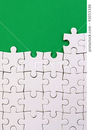 Fragment of a folded white jigsaw puzzle on the background of a green plastic surface. Texture photo with copy space for text Fragment of a folded white jigsaw puzzle on the background of a green plastic surface. Texture photo with copy space for text 93053386