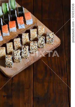 Sushi set of a number of rolls is located on a wooden cutting board on a table in the kitchen of a sushi bar. A traditional dish of oriental cuisine Sushi set of a number of rolls is located on a wooden cutting board on a table in the kitchen of a sushi bar. A traditional dish of oriental cuisine 93053936