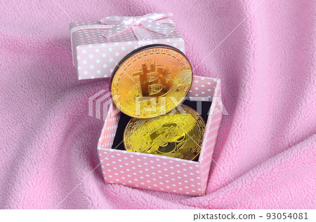 The golden bitcoin lies in a small pink gift box with a small bow on a blanket made of soft and fluffy light pink fleece fabric with a large number of relief folds The golden bitcoin lies in a small pink gift box with a small bow on a blanket made of soft and fluffy light pink fleece fabric with a large number of relief folds 93054081