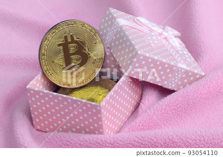 The golden bitcoin lies in a small pink gift box with a small bow on a blanket made of soft and fluffy light pink fleece fabric with a large number of relief folds The golden bitcoin lies in a small pink gift box with a small bow on a blanket made of soft and fluffy light pink fleece fabric with a large number of relief folds 93054110