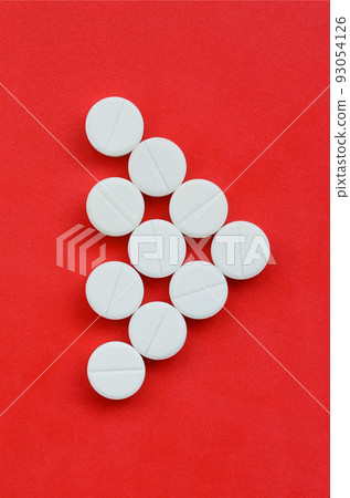 Several white tablets lie on a bright red background in the form of a triangular arrow. Background image on medicine and pharmaceutical topics Several white tablets lie on a bright red background in the form of a triangular arrow. Background image on medicine and pharmaceutical topics 93054126