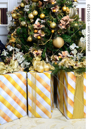 Photo of luxury gift boxes under Christmas tree, New Year home decorations, golden wrapping of Santa presents, festive fir tree decorated with garland, baubles and toys, traditional celebration Photo of luxury gift boxes under Christmas tree, New Year home decorations, golden wrapping of Santa presents, festive fir tree decorated with garland, baubles and toys, traditional celebration 93054129