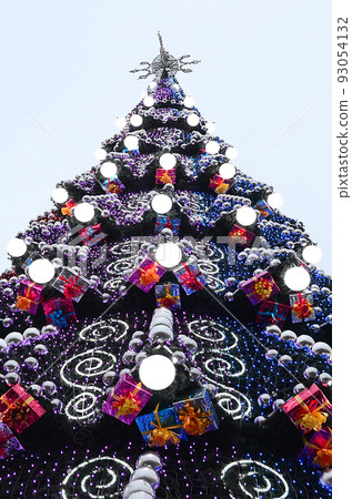 A fragment of a huge Christmas tree with many ornaments, gift boxes and luminous lamps. Photo of a decorated Christmas tree close-up with copy space A fragment of a huge Christmas tree with many ornaments, gift boxes and luminous lamps. Photo of a decorated Christmas tree close-up with copy space 93054132