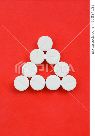 Several white tablets lie on a bright red background in the form of an even triangle. Background image on medicine and pharmaceutical topics 93054155