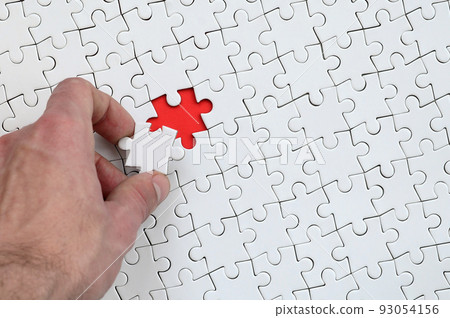 The texture of a white puzzle puzzle in the assembled state with one missing element that the male hand puts in The texture of a white puzzle puzzle in the assembled state with one missing element that the male hand puts in 93054156