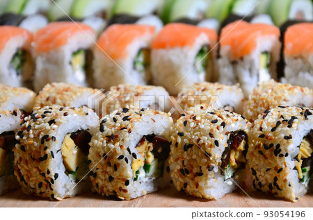 A macro shot of a sushi set of many rolls is located on a wooden cutting board on a table in the kitchen of a sushi bar. A traditional dish of Japanese cuisine 93054196