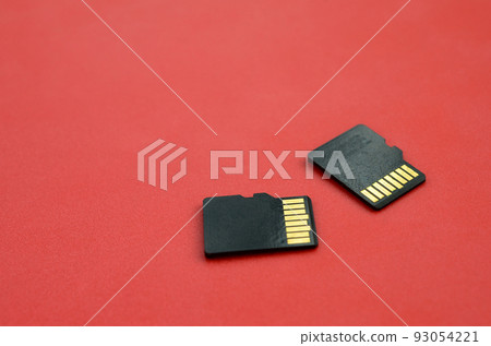 Two small micro SD memory cards lie on a red background. A small and compact data and information store 93054221