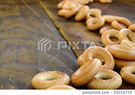 A lot of fresh yellow bagels lie on the surface of the old dark wood. A popular kind of flour products. One of the traditional Russian treats for tea A lot of fresh yellow bagels lie on the surface of the old dark wood. A popular kind of flour products. One of the traditional Russian treats for tea 93054259