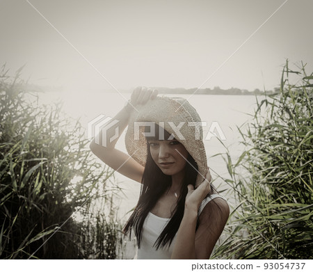 Young woman in vintage hat standing next to riverside with reeds, copyspace on sky Young woman in vintage hat standing next to riverside with reeds, copyspace on sky 93054737