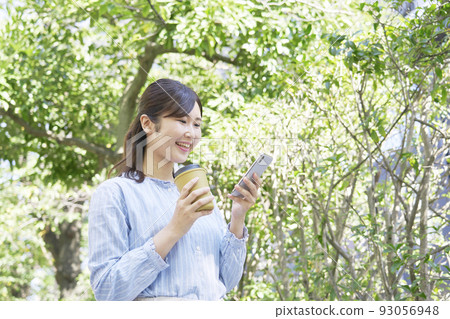 A woman using a smartphone with a smile outdoors A woman using a smartphone with a smile outdoors 93056948