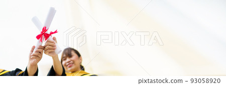 Happy Asian graduate student holding the diplomas on hand during the university graduation ceremony. Master degree student in gown suit holding a diplomas for photography. 93058920