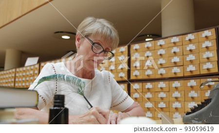 4K. An elderly woman writes a letter in the library 93059619