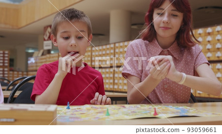 4K. Children play a board game in the library, sitting at the table. 93059661
