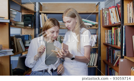 4K. Young female students choose a book to read in the college library. 93059714