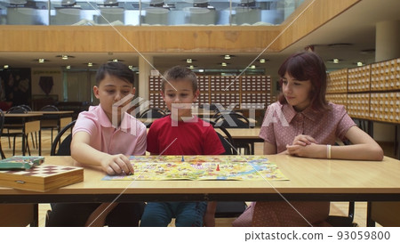 4K. Children play a board game in the library, sitting at the table. 93059800