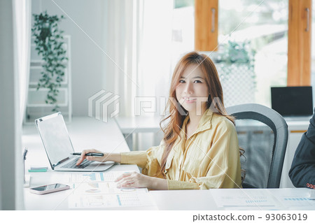 Female accountant using calculator and talking on telephone while sitting in an office. 93063019