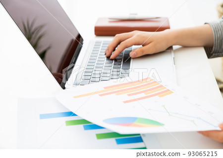A young woman in the office working on a computer while looking at a graph 93065215
