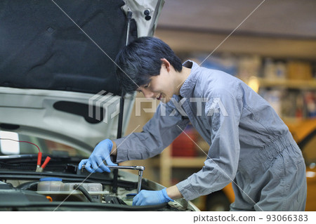 An auto mechanic inspecting the inside of the hood 93066383