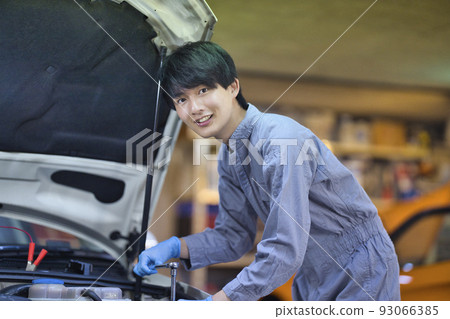 An auto mechanic inspecting the inside of the hood 93066385
