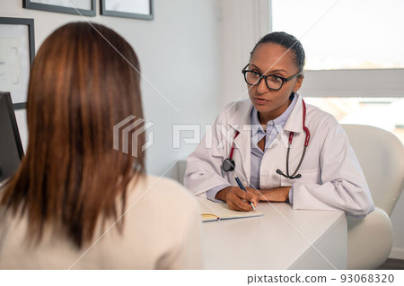 Confident doctor writing symptoms of female patient in notebook 93068320