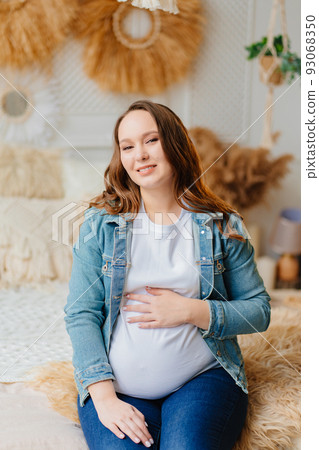 a beautiful pregnant woman in jeans sitting on the bed 93068350